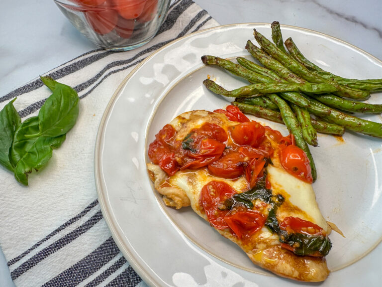 Chicken caprese with a seared chicken breast, melted mozzarella cheese, tomatoes, sliced basil, and a drizzle of balsamic vinegar with a side of fresh roasted green beans.