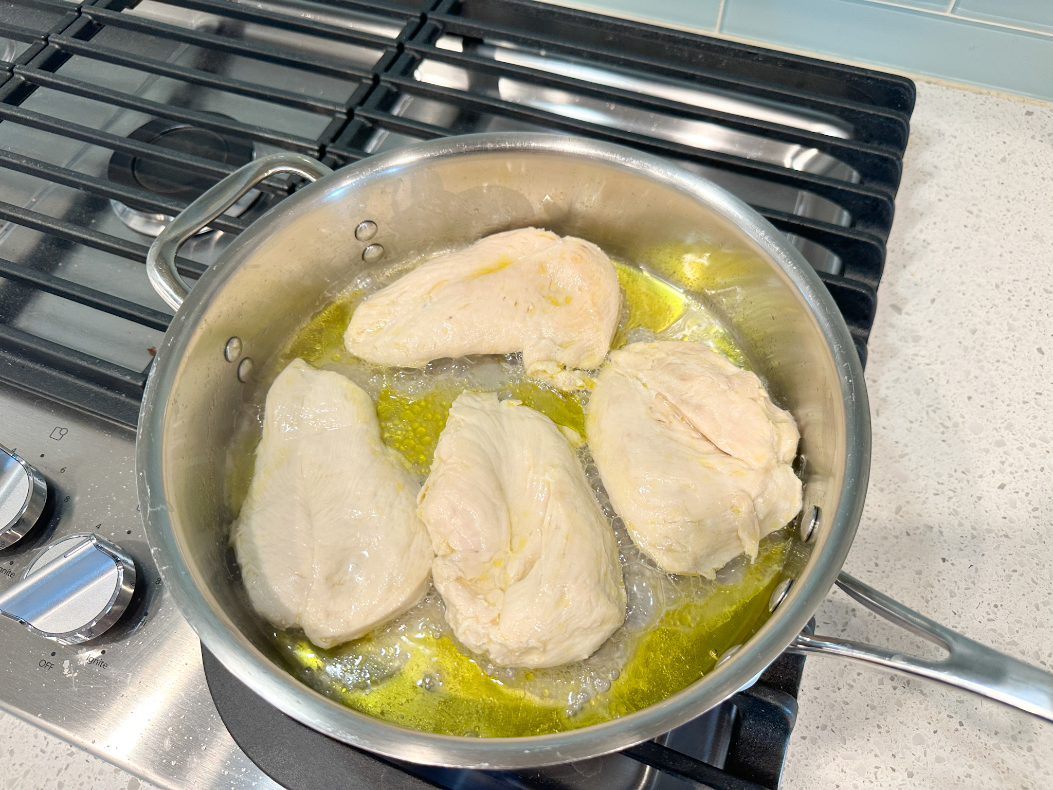 4 chicken breasts frying in a skillet on the stove.