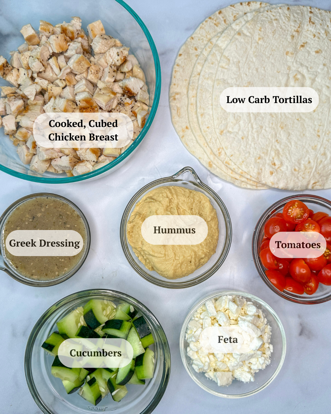 Grilled Greek Chicken Wrap ingredients: tortillas, diced tomatoes, diced cucumbers, crumbled feta cheese, hummus, Greek dressing, cubed cooked chicken breast