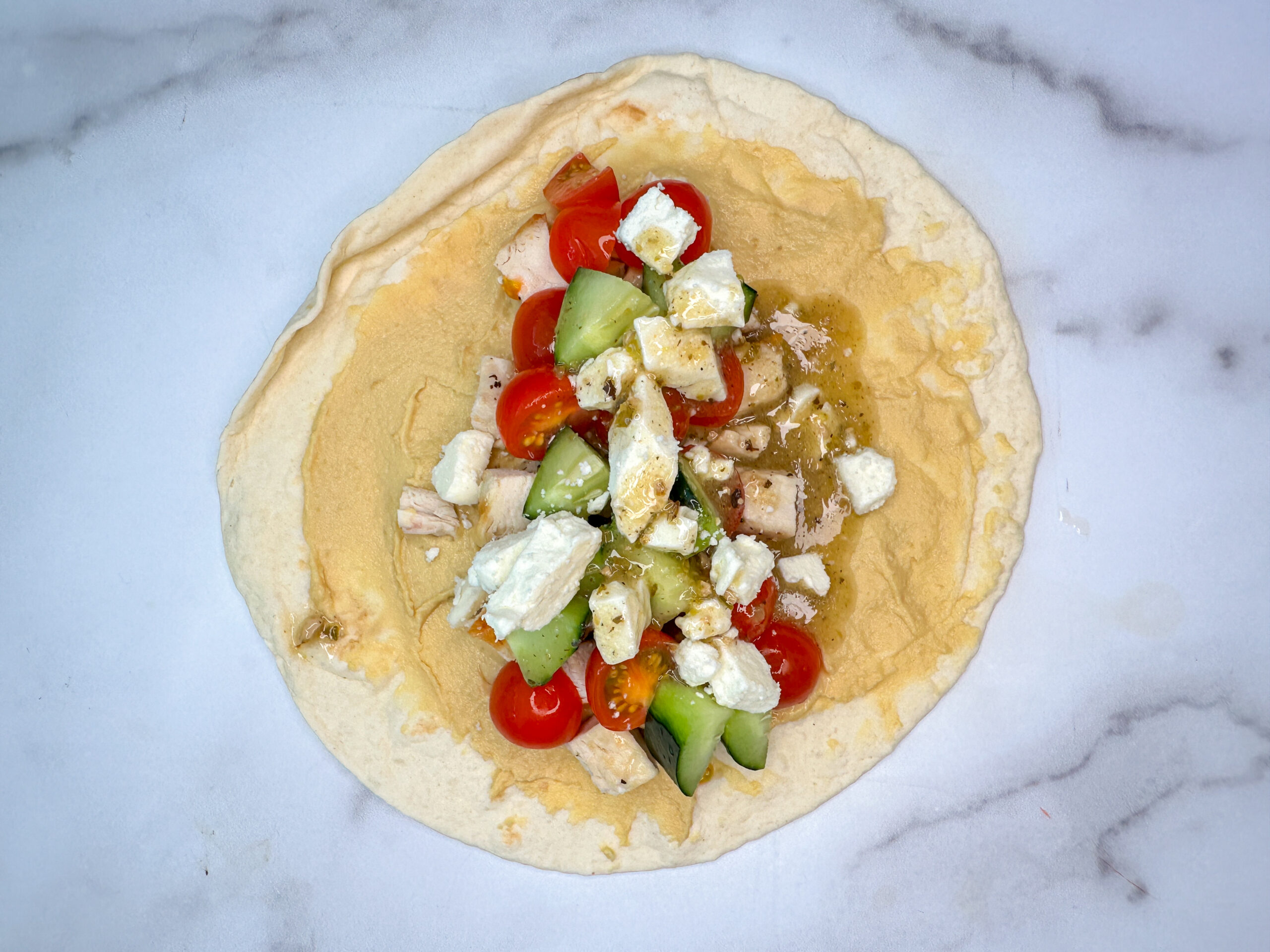 Grilled Greek Wrap with tortilla, hummus, and chicken, cucumbers, tomatoes, and feta on top.