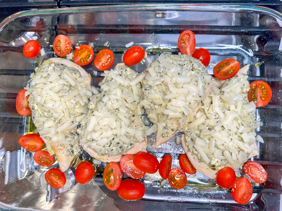 4 Grilled chicken breasts topped with cream cheese and basil mixture and topped with shredded mozzarella with sliced cherry tomatoes in a glass baking dish