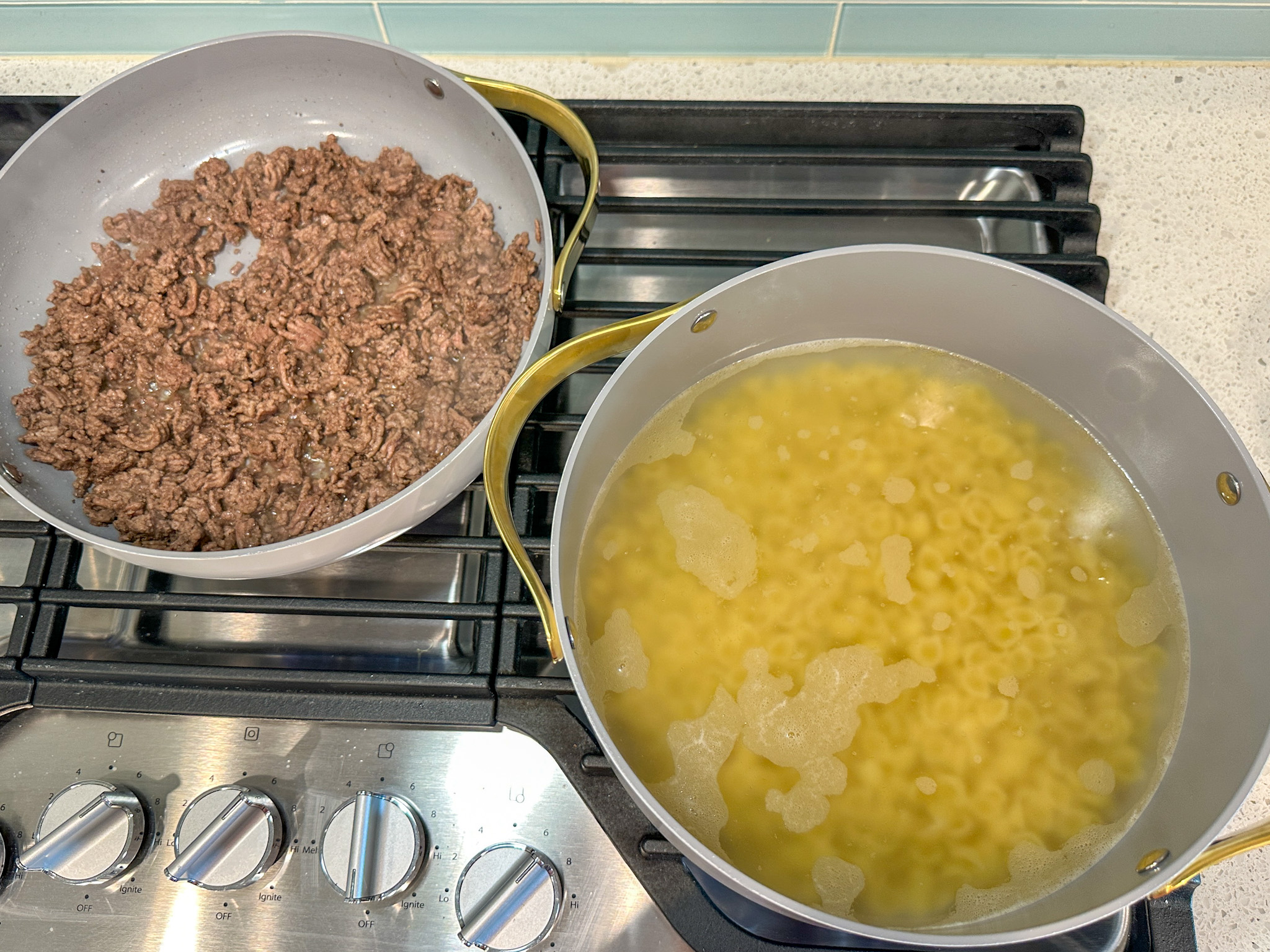 Noodles boiling in a pot on the stove and ground beef cooking in a skillet on the stove.