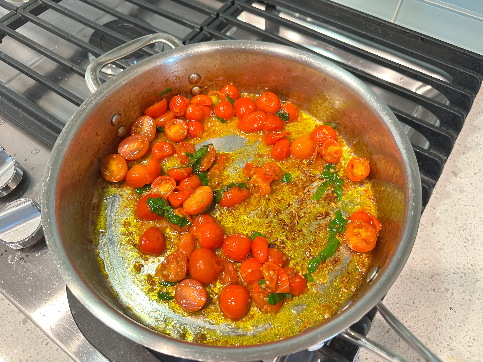 cherry tomatoes sauteeing in a skillet with olive oil.