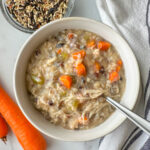 a bowl of chicken and wild rice soup with 2 carrots to the side and a small bowl of wild rice close by.