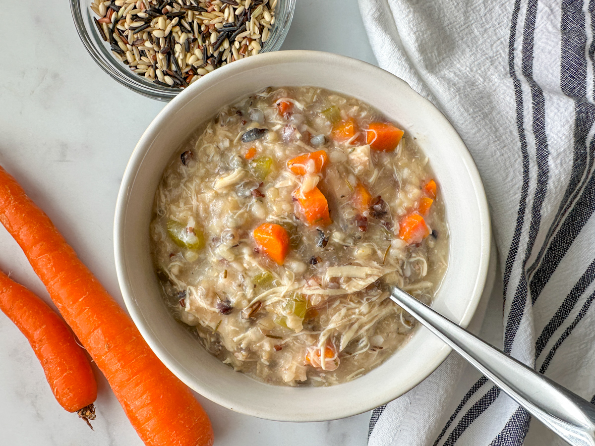 a bowl of chicken and wild rice soup with 2 carrots to the side and a small bowl of wild rice. 