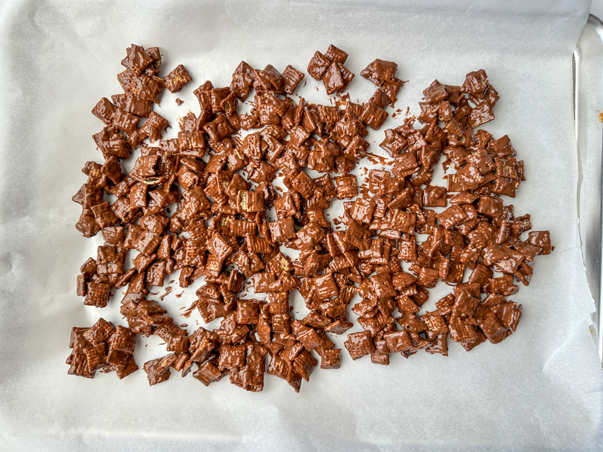 Puppy chow chex mix with peanut butter chocolate spread on parchment paper drying.