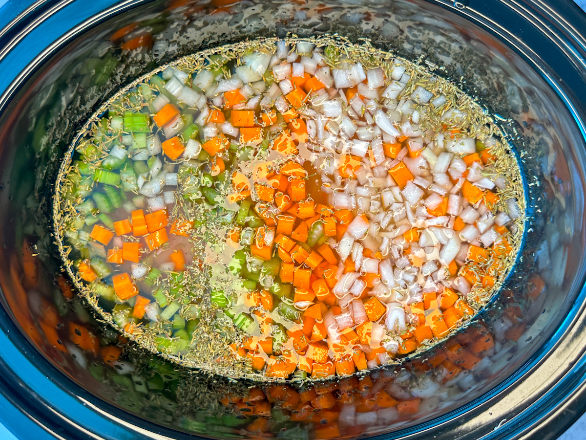 Crockpot filled with chopped celery, carrots, onion, raw chicken breasts, wild rice, and seasonings.