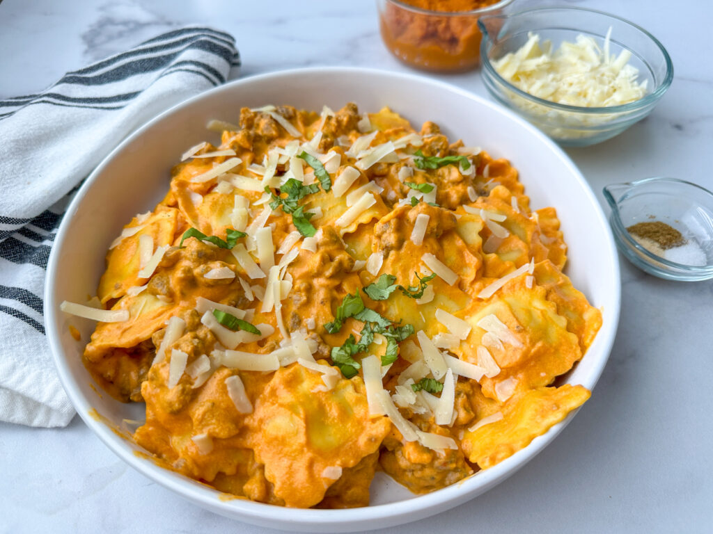 Creamy pumpkin ravioli with sausage on a plate topped with shredded parmesan cheese and basil.