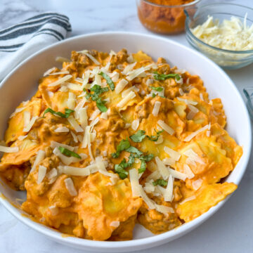Creamy pumpkin ravioli with sausage on a plate topped with shredded parmesan cheese and basil.