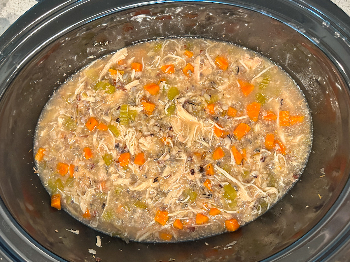 Crockpot filled with cooked wild rice, chopped carrots, celery, and onions, cooked shredded chicken, and seasonings.