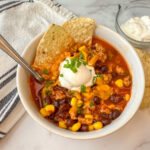 White bowl filled with easy turkey taco soup with a dollop of sour cream and sliced green onions on top with 2 tortilla chips as garnish.