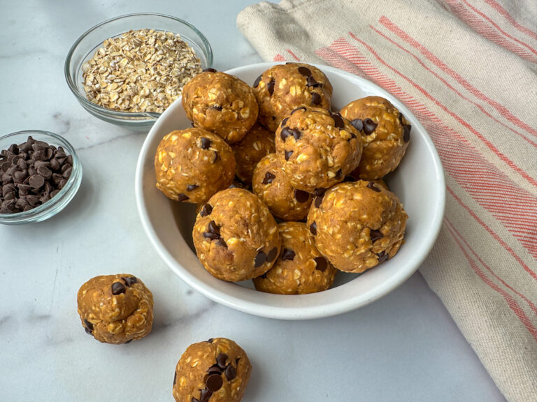 12 Protein Pumpkin Balls in a white bowl with a small bowl of mini chocolate chips and a bowl of oats.