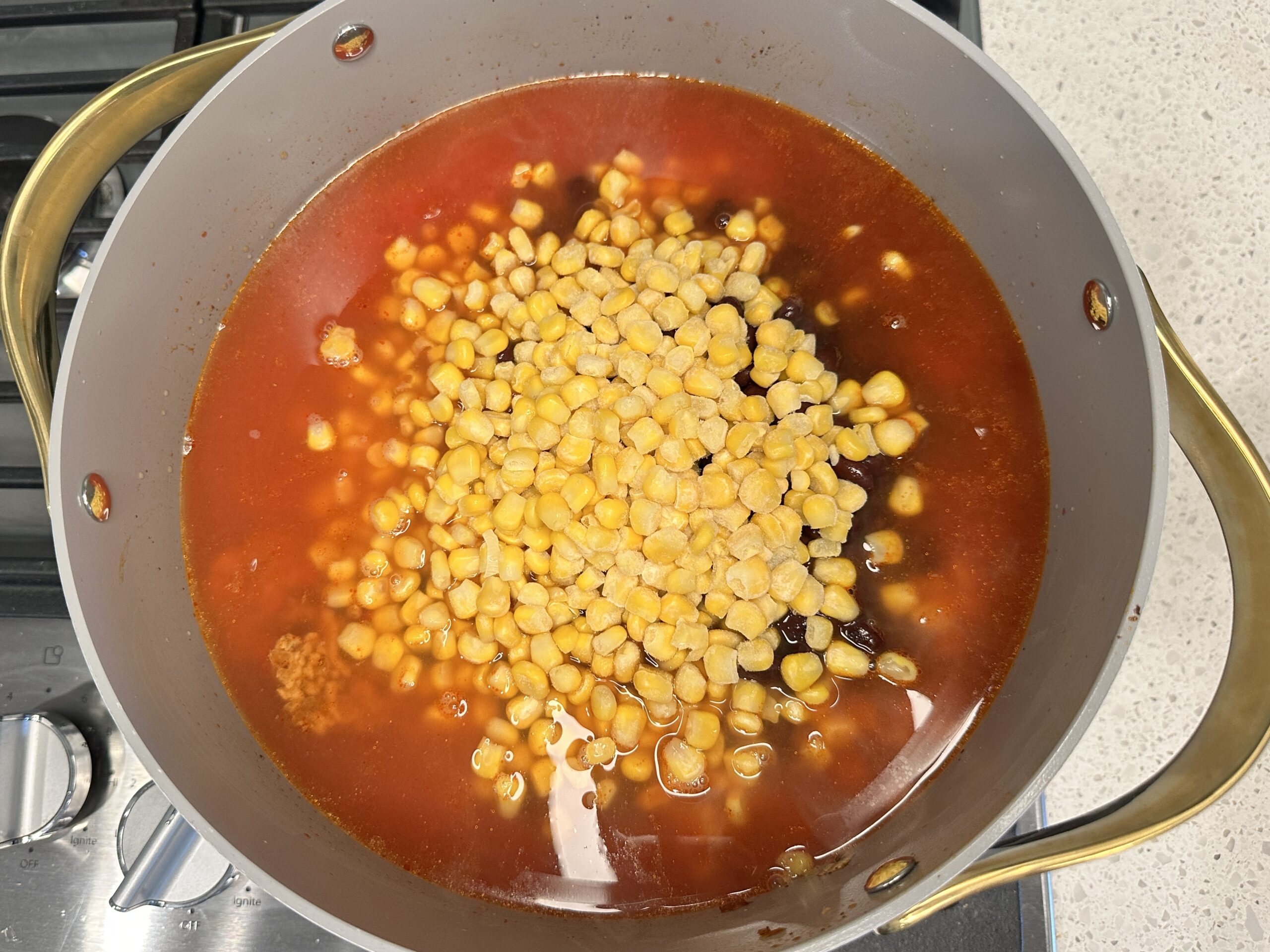 Turkey Taco Soup ingredients in a large pot: crushed tomatoes, chicken broth, frozen corn, black beans, ground turkey, spices.
