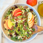 a large white bowl filled with a fall brussels sprouts and apple salad with shredded brussels, chopped kale, sliced apples, and dried cranberries.
