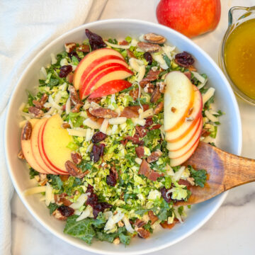 a large white bowl filled with a fall brussels sprouts and apple salad with shredded brussels, chopped kale, sliced apples, and dried cranberries.