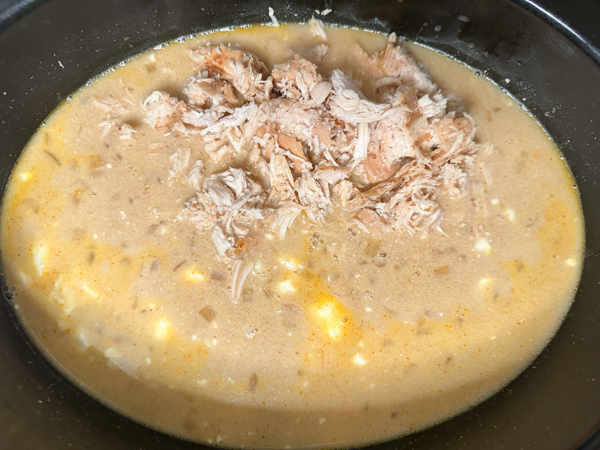 Creamy chicken chili liquid and beans with cooked, shredded chicken added to the top.