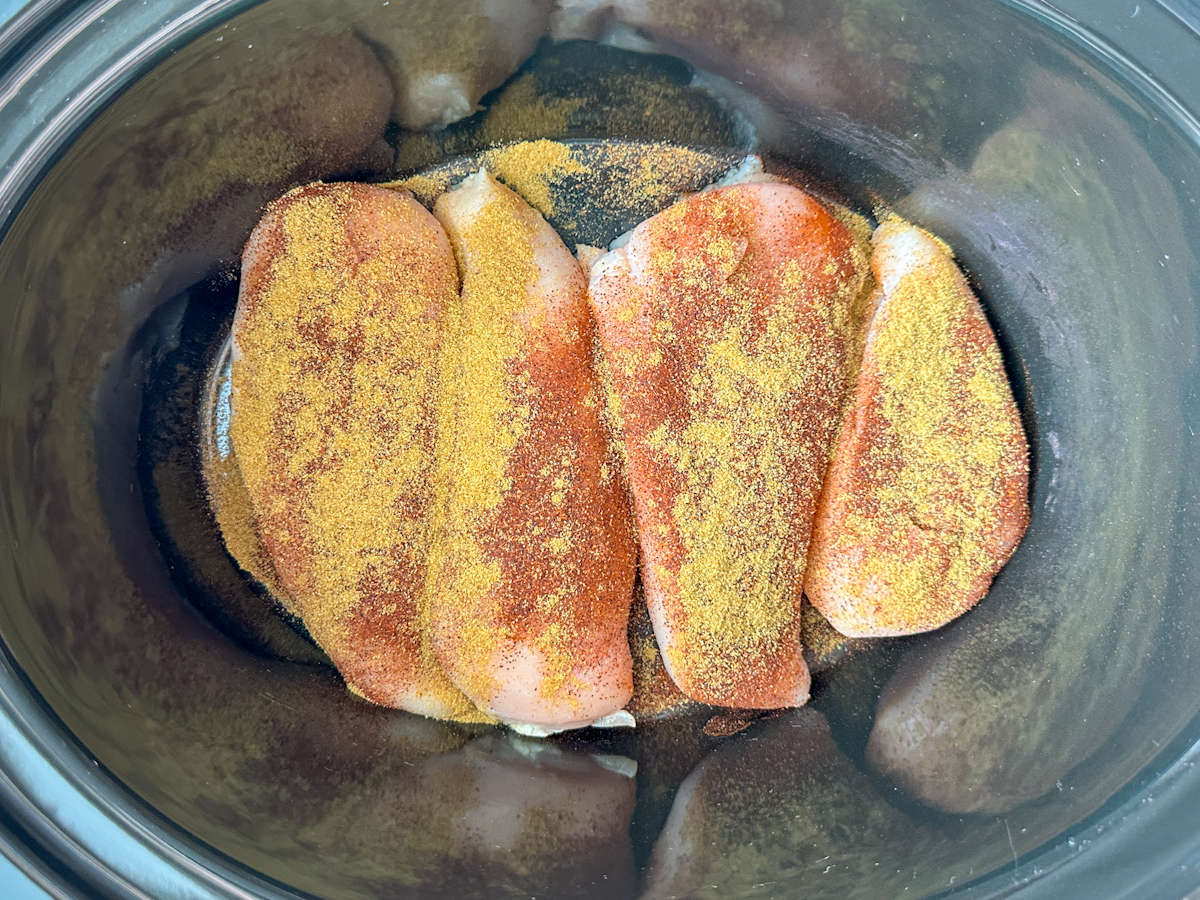 4 chicken breasts in a crockpot with chili powder and cumin sprinkled on top.
