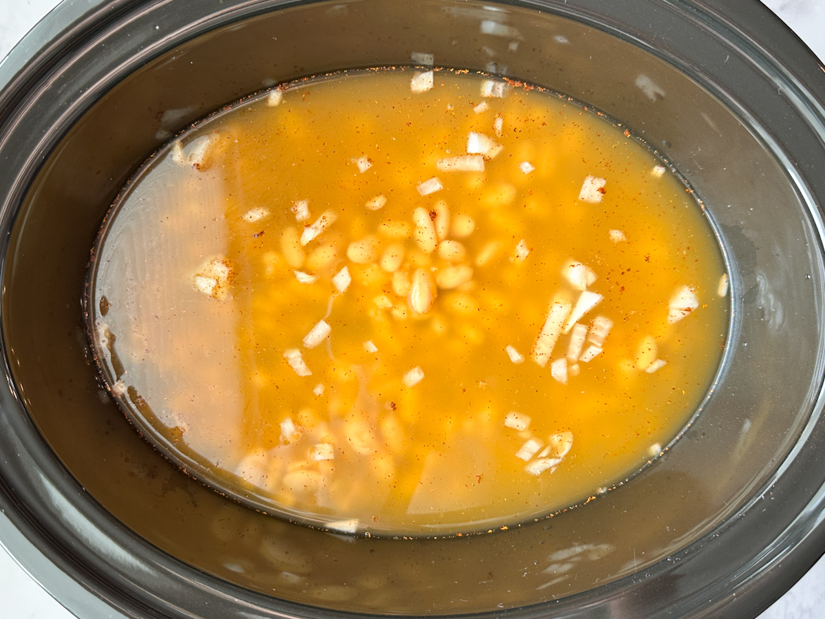 4 chicken breasts topped with chicken broth, chili powder, diced onions, and white chili beans.