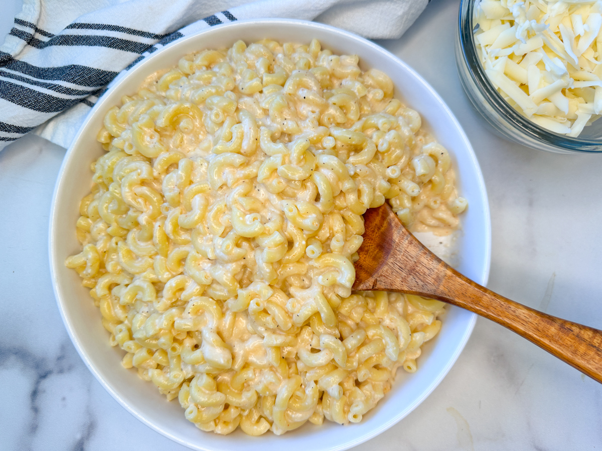 High Protein Mac and Cheese in a large bowl with a side of shredded white cheddar.