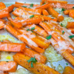 Quartered carrot sticks with melted parmesan cheese topped with chopped parsley on a baking sheet.