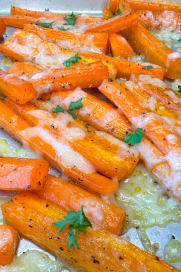 Quartered carrot sticks with melted parmesan cheese topped with chopped parsley on a baking sheet.