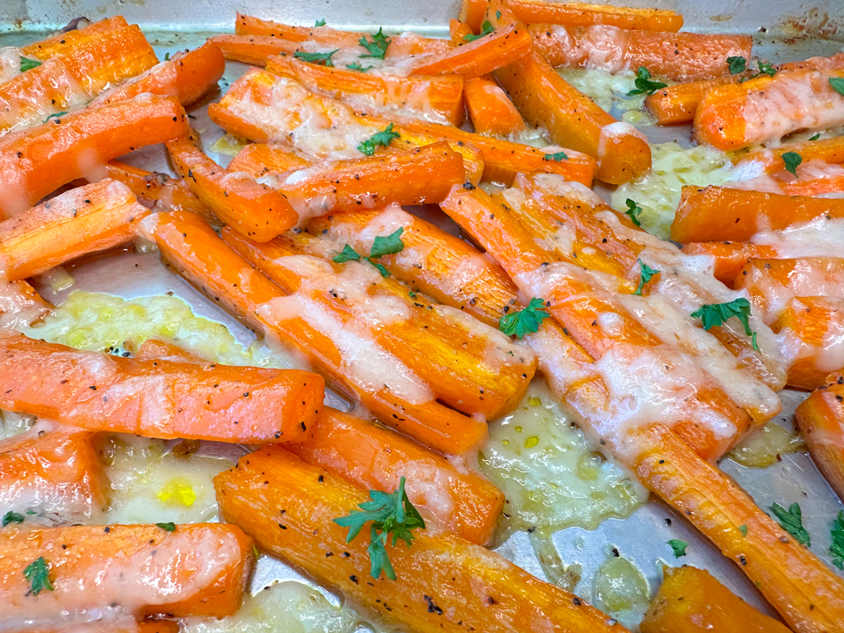 Parmesan Roasted Carrots on a baking sheet with melted parmesan cheese and topped with parsley.