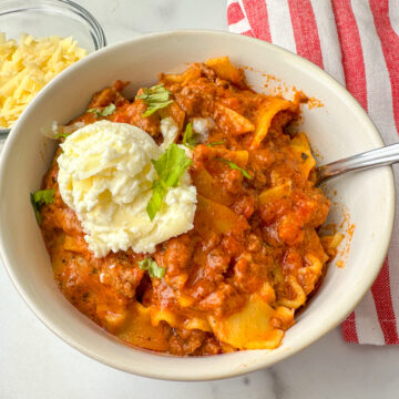 bowl of lasagna soup with cooked lasagna noodle pieces, cooked ground beef, tomato sauce, and a dollop of ricotta cheese on top.