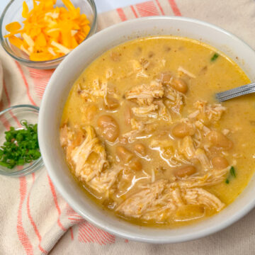 white chicken chili in a white bowl topped with sliced green onions.