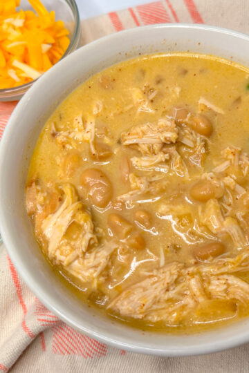 white chicken chili in a white bowl topped with sliced green onions.