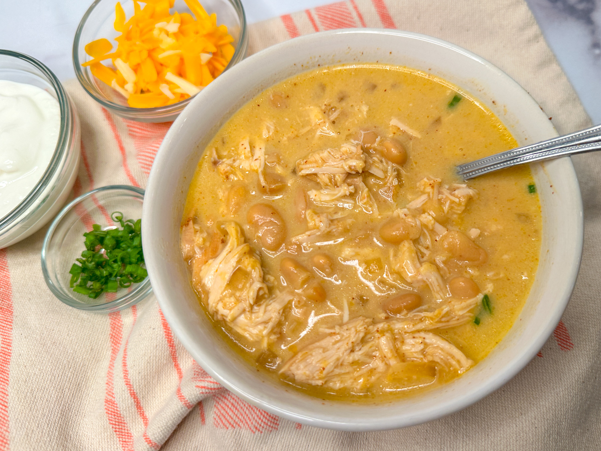white chicken chili in a white bowl topped with sliced green onions.