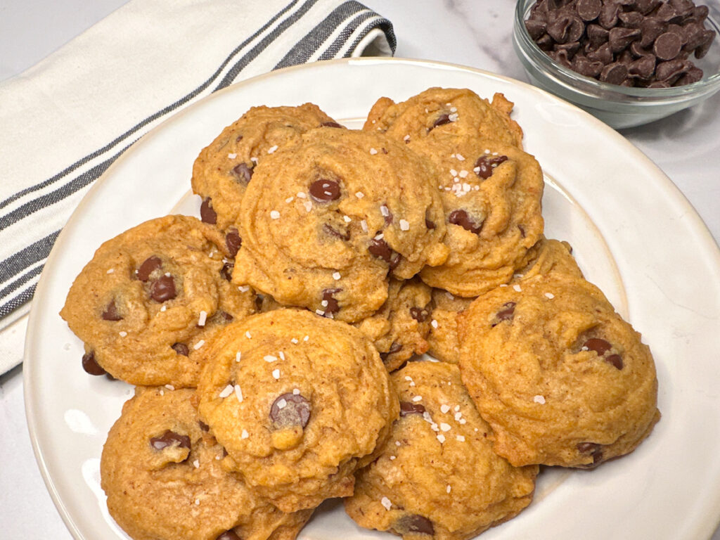 1 dozen brown butter pumpkin chocolate chip cookies piled on a plate topped with coarse sea salt.