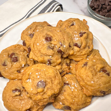 1 dozen brown butter pumpkin chocolate chip cookies piled on a plate topped with coarse sea salt.