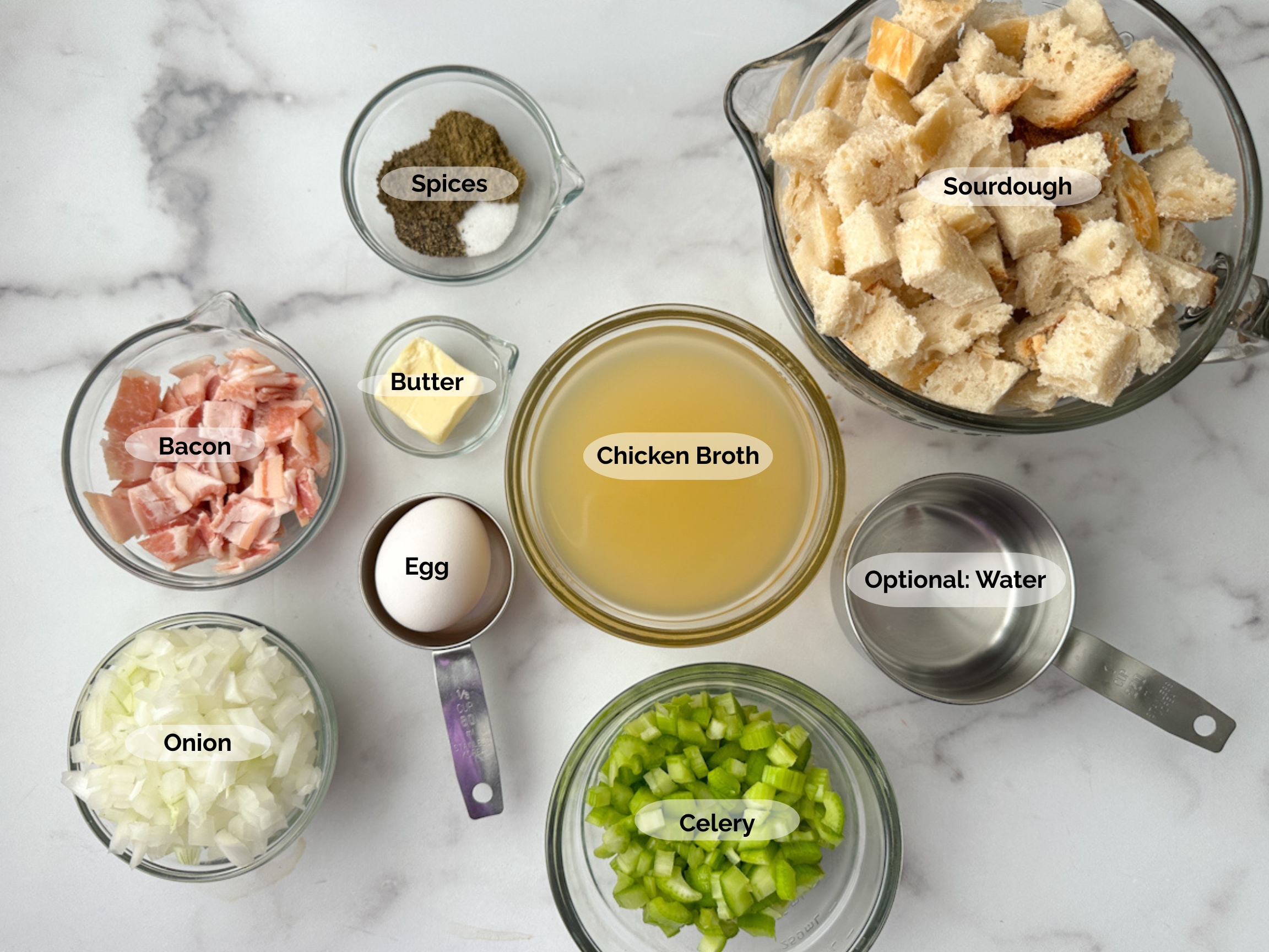 Sourdough Stuffing ingredients: sourdough cubes, spices, bacon, diced onions, diced celery, egg, butter, chicken broth, and optional water.