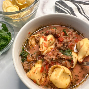 tuscan tortellini soup in a bowl with cheese tortellini pastas in a tomato broth soup with cooked ground sausage.