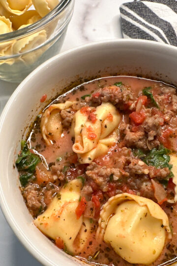 tuscan tortellini soup in a bowl with cheese tortellini pastas in a tomato broth soup with cooked ground sausage.