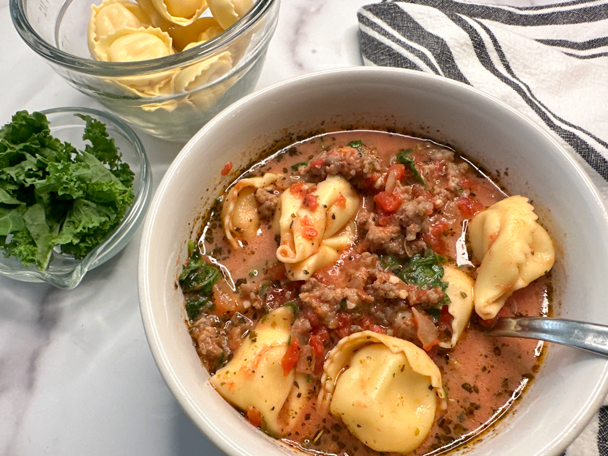 Tuscan Tortellini Soup in a bowl with a side of kale and tortellini. A few tortellini pastas with cooked ground sausage in a tomato broth soup.
