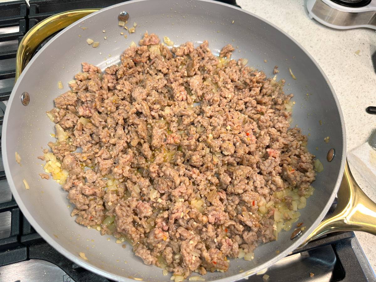 Ground Italian sausage cooked with chopped onion in a large skillet.