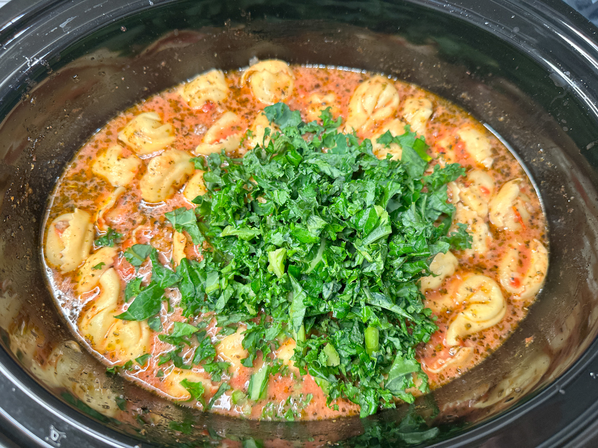 Tuscan Tortellini Soup topped with chopped kale in a crockpot.