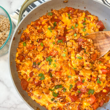 Cooked unstuffed pepper skillet meal in a large skillet with a side of rice. Cooked turkey with chopped cooked peppers, shredded, melted cheese, and diced tomatoes topped with sliced green onions.