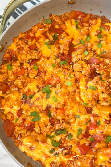 Cooked unstuffed pepper skillet meal in a large skillet with a side of rice. Cooked turkey with chopped cooked peppers, shredded, melted cheese, and diced tomatoes topped with sliced green onions.