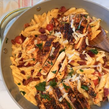 Creamy Bacon and Chicken Pasta in a large skillet with cooked, cheesy noodles topped with crumbled bacon and melty cheese.