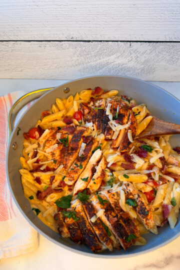 Creamy bacon and chicken pasta cooked in a large skillet with cooked noodles in a cheesy sauce topped with grilled chicken and crumbled bacon.