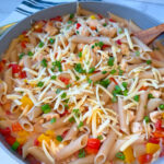 Creamy Cajun Chicken Pasta in a large skillet with cooked cubed chicken, penne, chopped bell peppers, and shredded parmesan with sliced green onions on top.