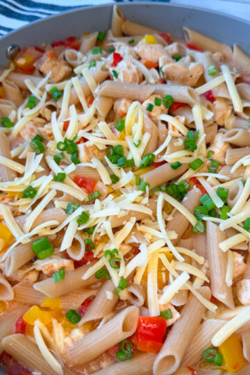 Creamy Cajun Chicken Pasta in a large skillet with cooked cubed chicken, penne, chopped bell peppers, and shredded parmesan with sliced green onions on top.