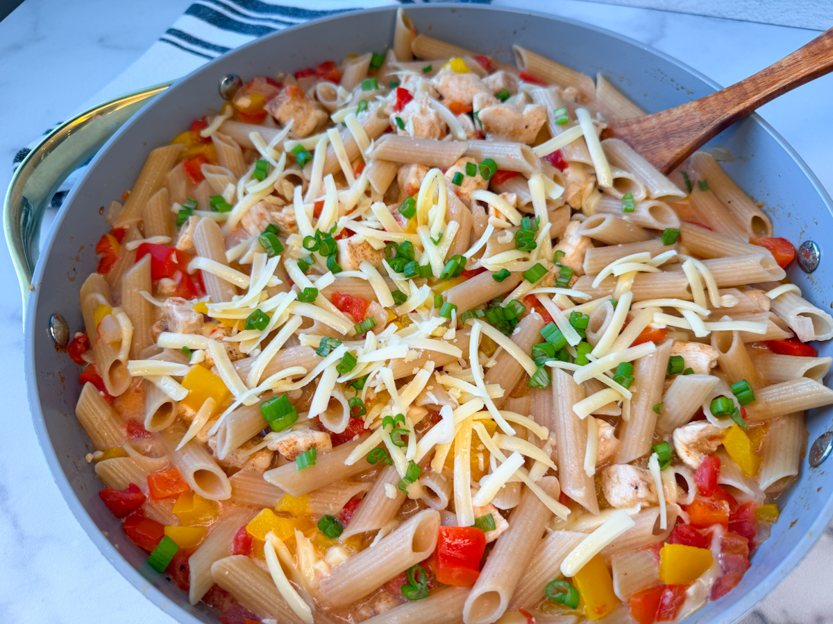 Creamy Cajun Chicken Pasta in a large non-stick skillet with penne noodles, chunks of chicken, and chopped red and yellow bell peppers. Topped with shredded parmesan and sliced green onions.