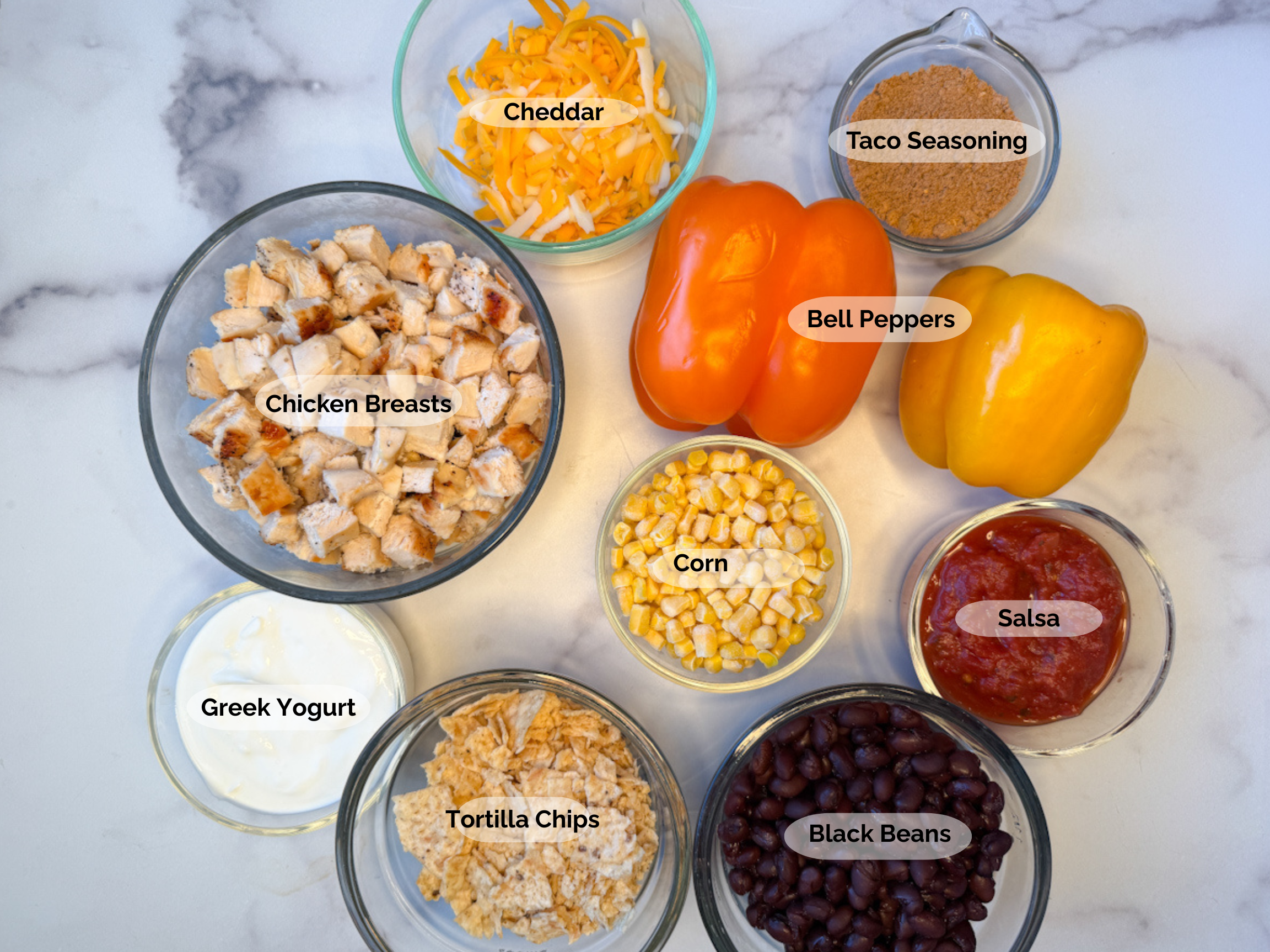 Healthy Chicken Taco Casserole ingredients: cooked cubed chicken breasts, shredded cheddar, orange and yellow bell peppers, taco seasoning, frozen corn, salsa, black beans, tortilla chips, greek yogurt