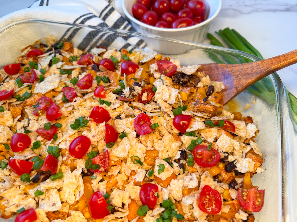 Healthy Chicken Taco Casserole in a glass baking dish topped with crushed tortilla chips, sliced green onions and quartered cherry tomatoes.