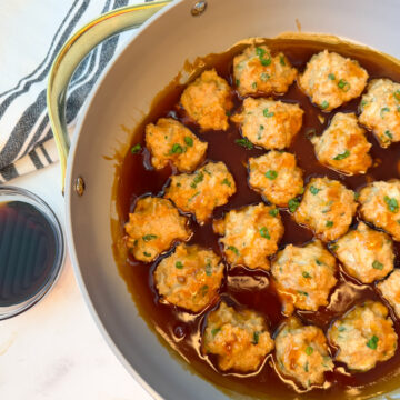 Several cooked chicken meatballs in a large skillet sitting in a teriyaki sauce
