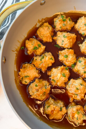 Several cooked chicken meatballs in a large skillet sitting in a teriyaki sauce
