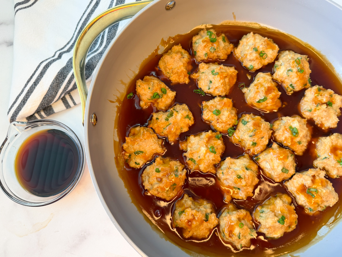 Several cooked chicken meatballs in a large skillet sitting in a teriyaki sauce